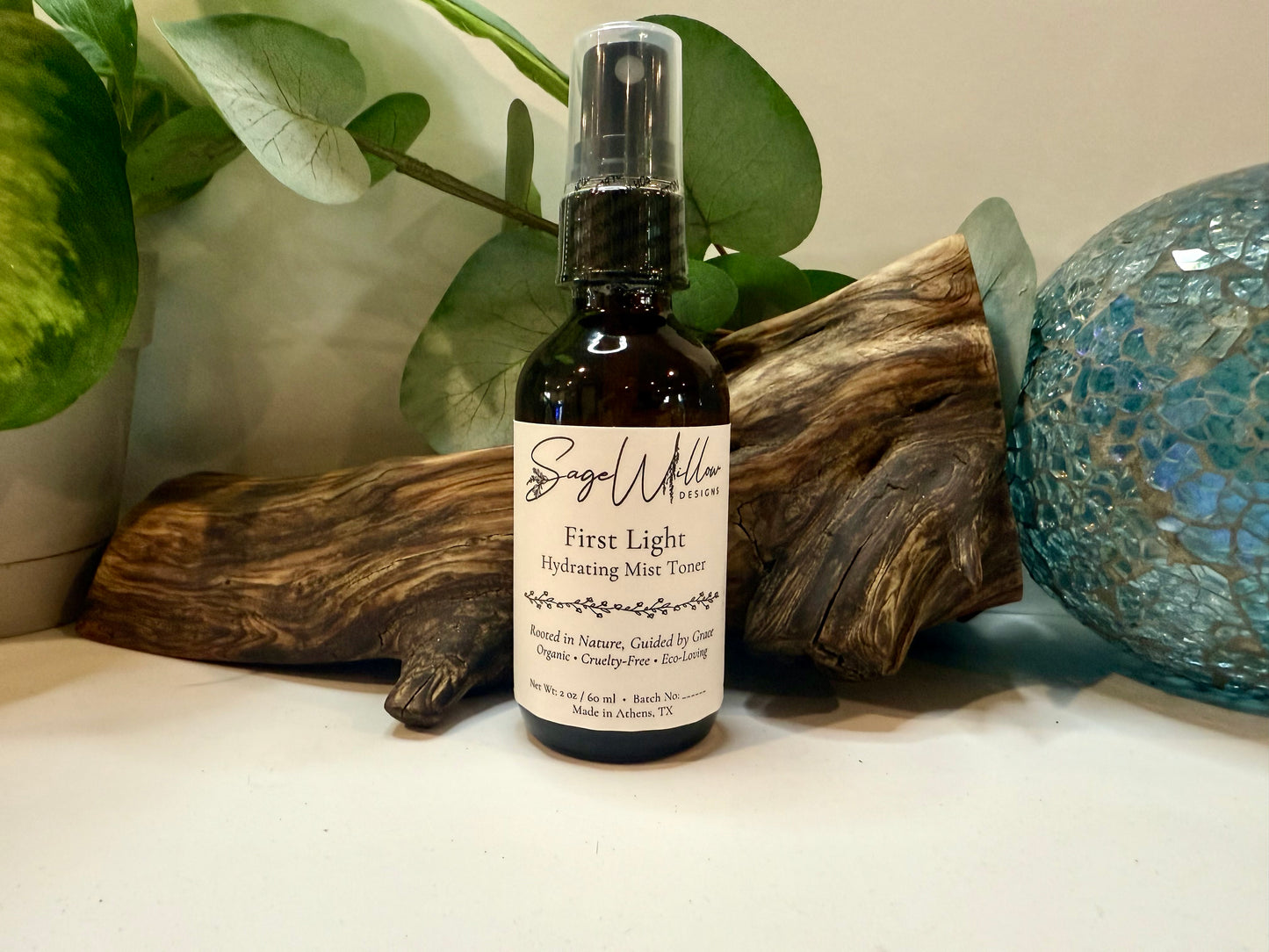 Bottle of 'First Light Hydrating Mist Toner' by Sage Willow on a surface with decorative elements.