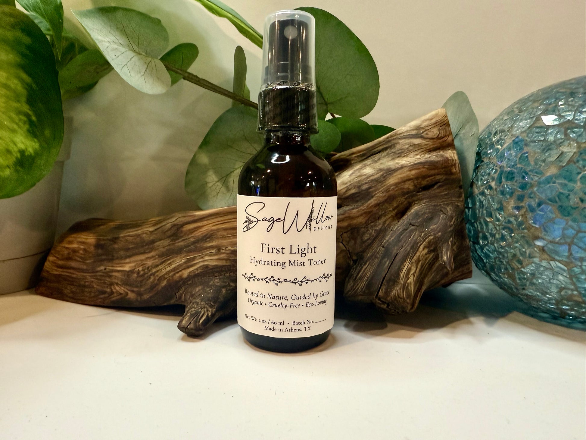 Bottle of 'First Light Hydrating Mist Toner' by Sage Willow on a surface with decorative elements.